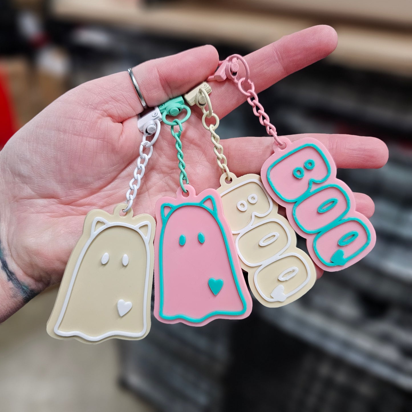 Hand holding a set of colorful keychains with 'BOO' text and ghost designs.