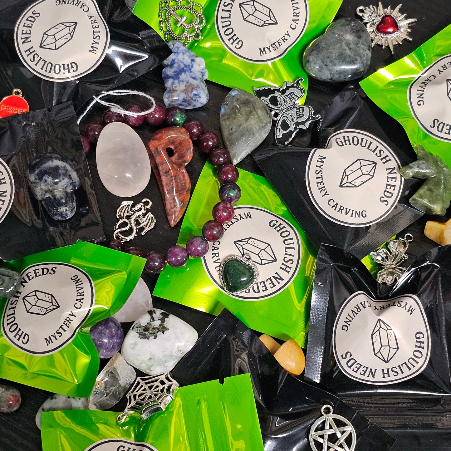 Collection of Ghoulish Needs mystery carving kit contents including stones, crystals, and jewelry on green packaging.