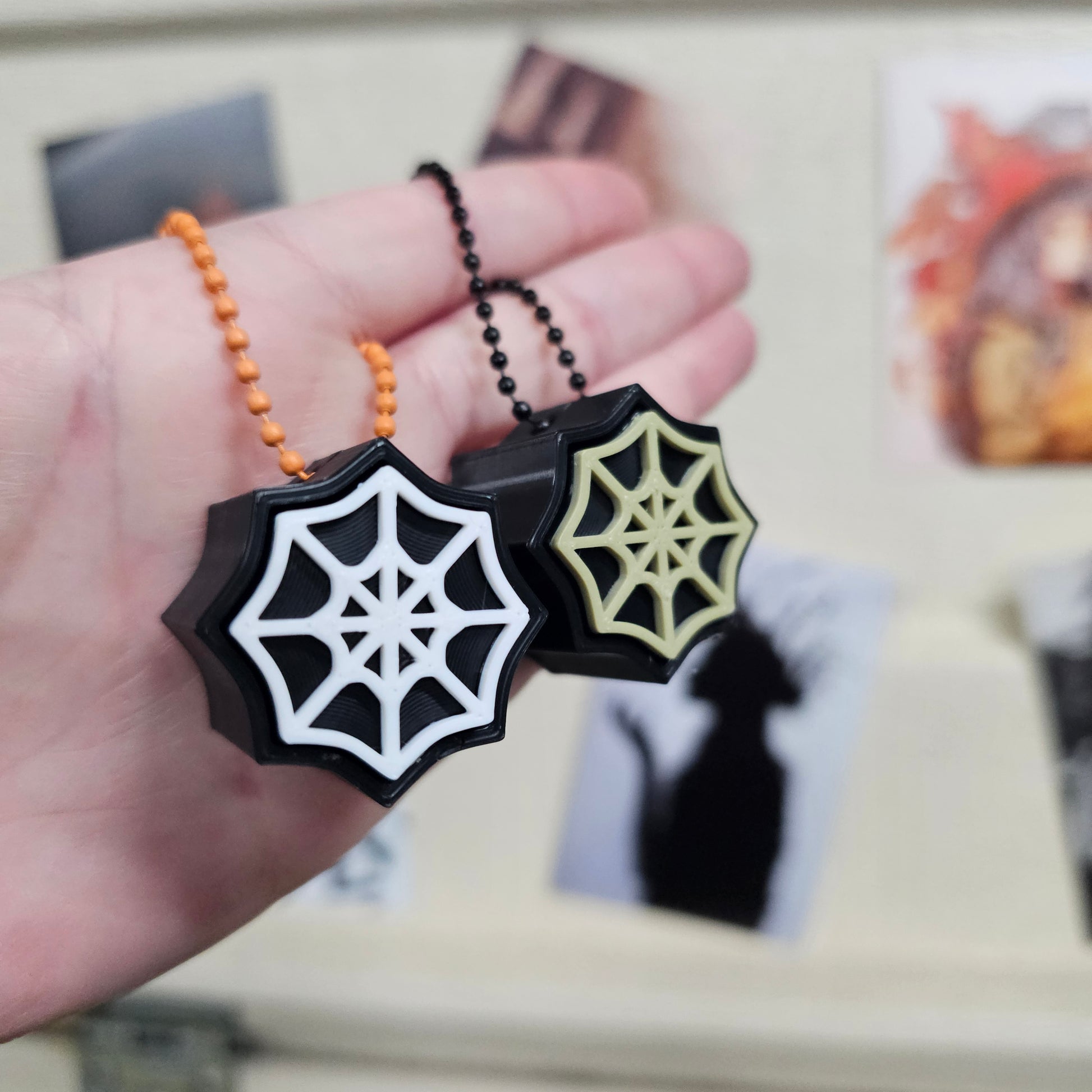 Spider web design keychains held in a hand with a blurred background