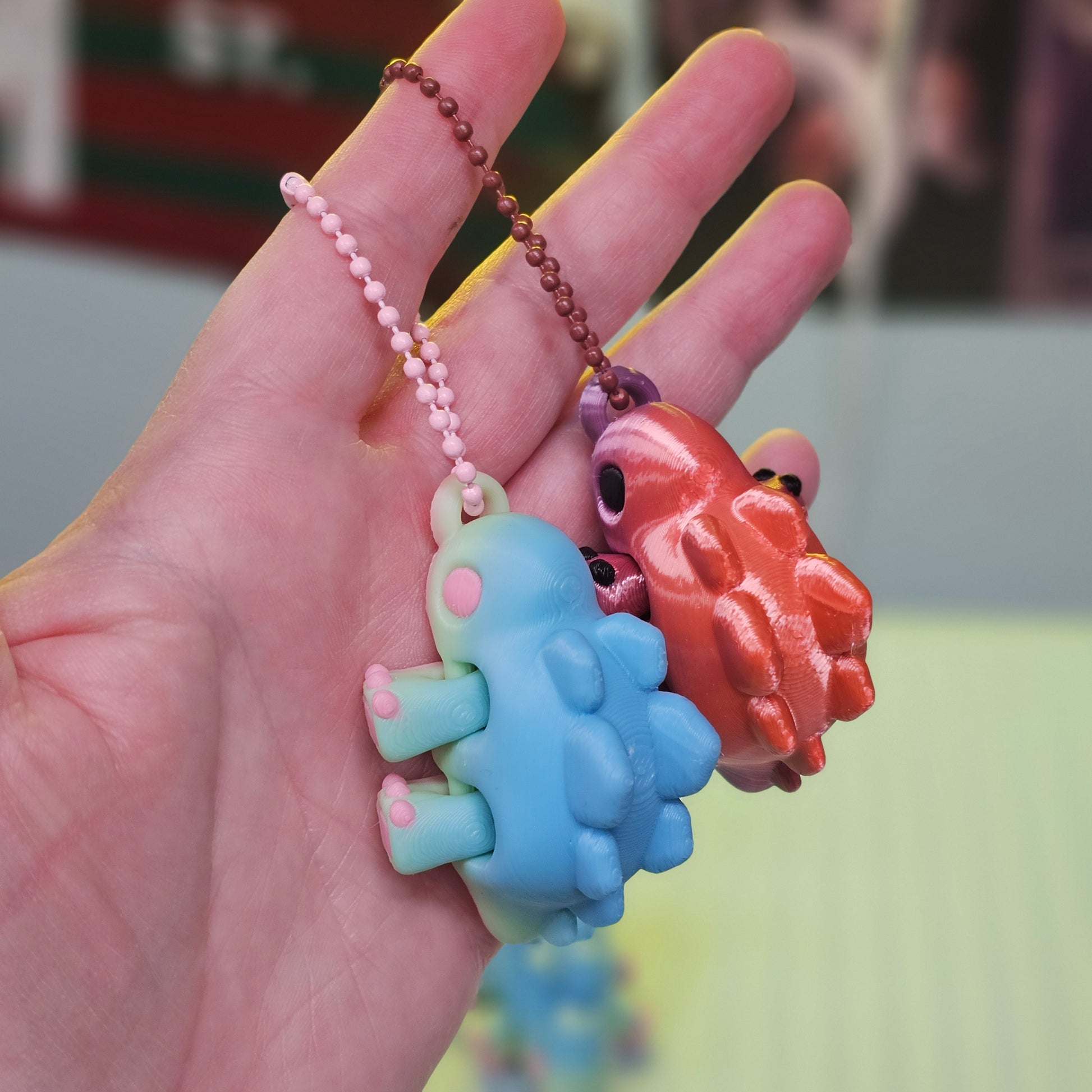 Two small dinosaur figurines on a chain held in a hand with a blurred background