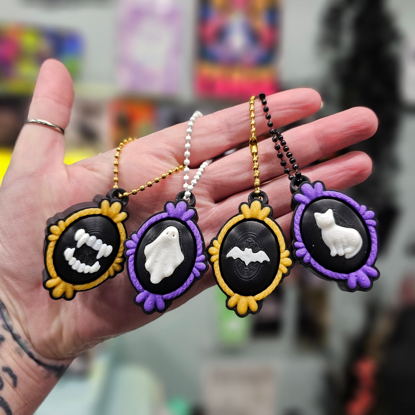 Hand holding three Halloween-themed keychains with ghost and bat designs on a blurred background.